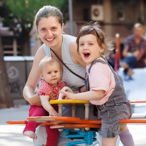 Happy woman with  two children on swings in city playground